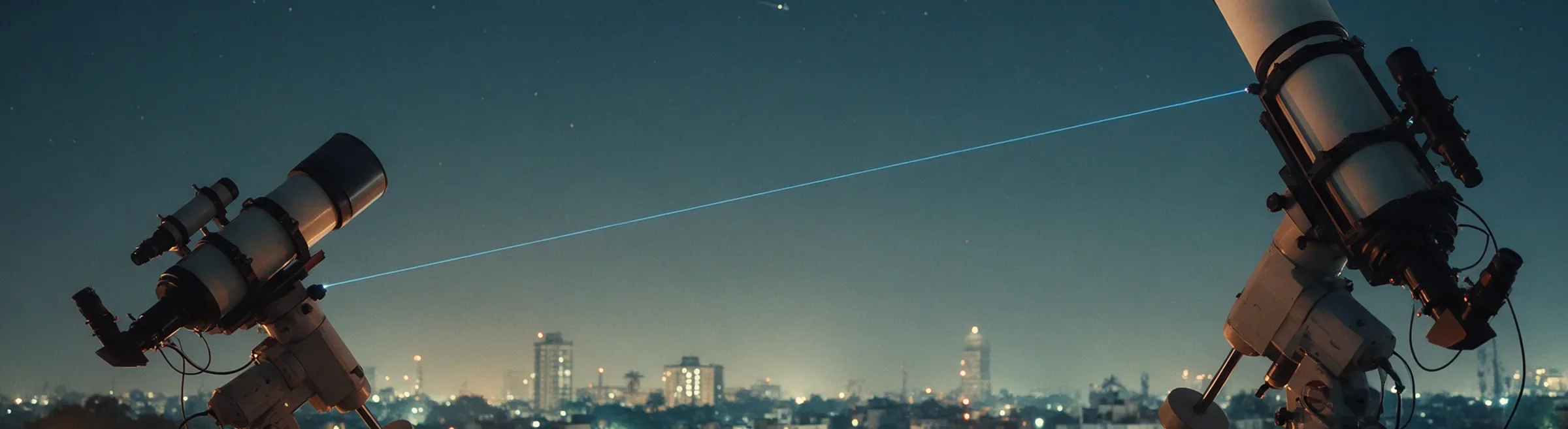 Two rooftop telescopes linked by a blue laser beam above a city at night